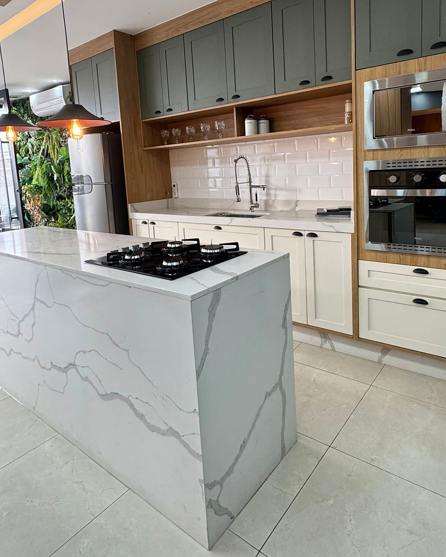 Cozinha planejada com ilha em quartzo, cooktop embutido e torre de fornos em inox